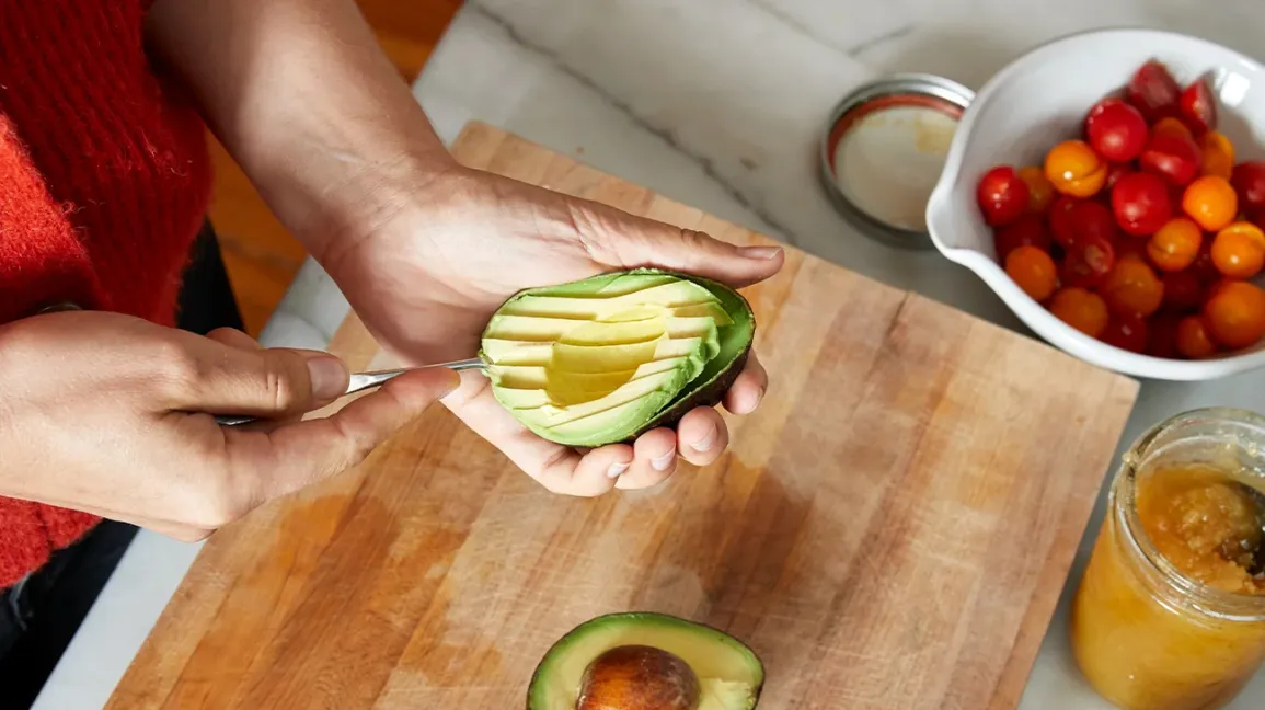 A person skillfully cuts an avocado on a cutting board