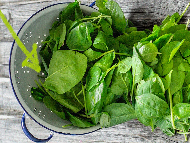 A colander filled with fresh spinach leaves